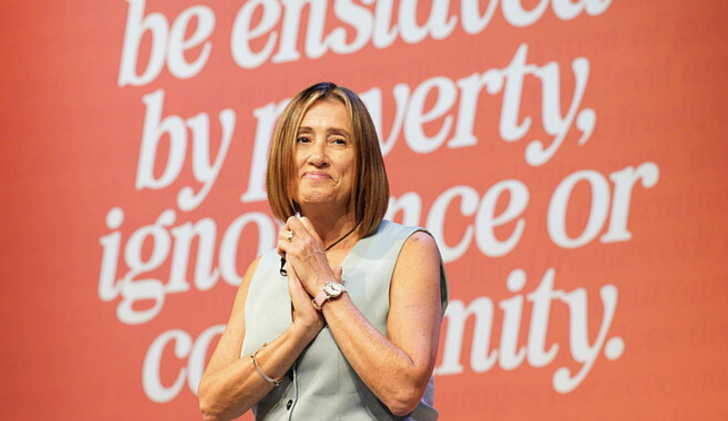 Jane Dodds on Conference stage in front of banner saying "none shall be enslaved by poverty, ignorance or conformity"